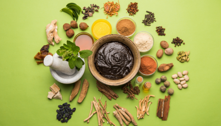 A jar of Chyawanprash with a spoonful of the herbal paste, surrounded by various herbs and spices, representing the health benefits of eating Chyawanprash as discussed in the blog.