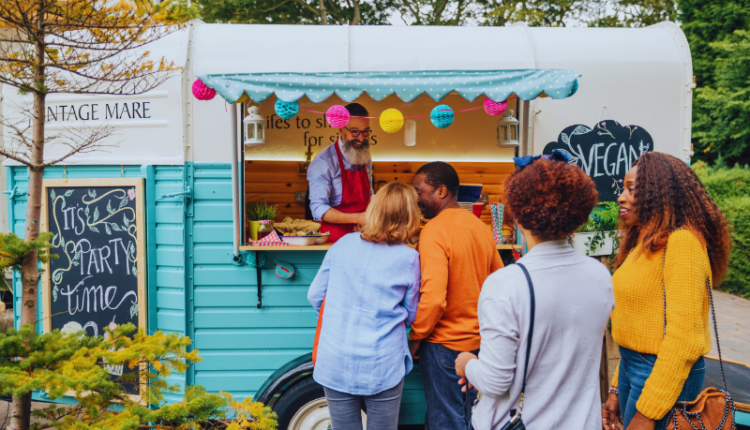How To Open A Food Truck Business : An illustration of a vibrant food truck parked on a busy street, serving customers with a variety of delicious meals. The image captures the bustling atmosphere, highlighting the food truck's colorful branding, open serving window, and a small crowd eagerly waiting to place orders. This visual represents the blog's focus on guiding aspiring entrepreneurs through the steps to successfully open and run a food truck business.